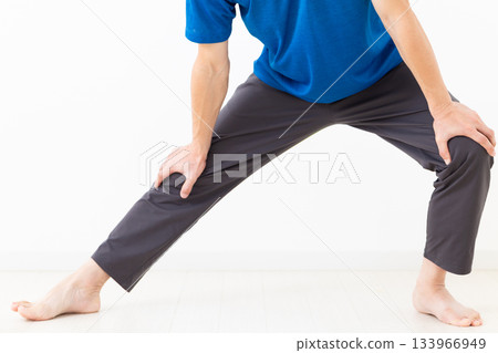 A middle-aged man in a T-shirt doing leg stretching exercises A middle-aged man in a T-shirt doing leg stretching exercises 133966949