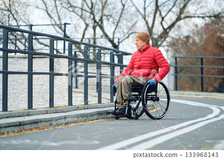 Senior man in wheelchair navigating a park path on a cool autumn day 133968143