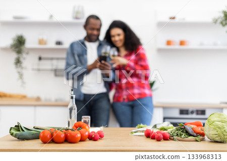 A couple enjoys a moment together in the kitchen, with fresh vegetables on the counter. A couple enjoys a moment together in the kitchen, with fresh vegetables on the counter. 133968313