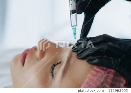 close up of professional hands making a rejuvenation injection into woman frown line close up of professional hands making a rejuvenation injection into woman frown line 133968905