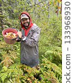 a man having a full bucket of pet mushroom in the forest.  133968930