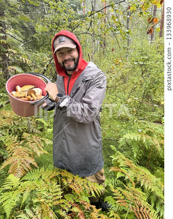 a man having a full bucket of pet mushroom in the forest. a man having a full bucket of pet mushroom in the forest. 133968930