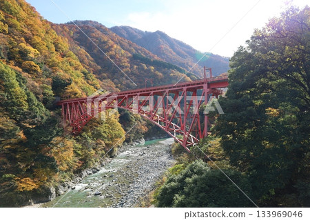 A red bridge and stream crossing the mountains of Unazuki Onsen, dyed in autumn leaves A red bridge and stream crossing the mountains of Unazuki Onsen, dyed in autumn leaves 133969046