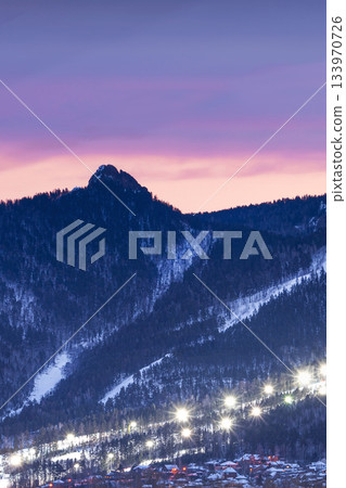 Evening panorama mountain ski resort. illuminated ski slope with burning lights during a beautiful lilac sunset. Evening panorama mountain ski resort. illuminated ski slope with burning lights during a beautiful lilac sunset. 133970726