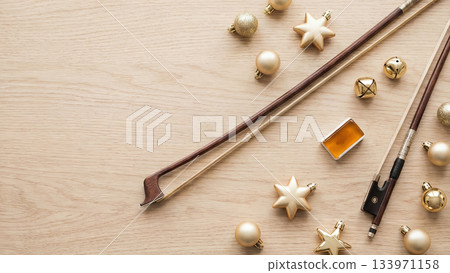 Top view of violin bows with gold baubles and stars on wood. Festive musical composition for holiday concerts invitation or greeting card. 133971158