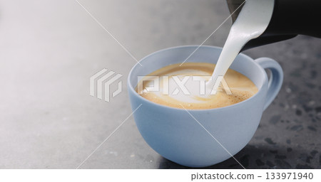 Pour steamed milk into espresso to make cappuccino in blue cup on concrete background Pour steamed milk into espresso to make cappuccino in blue cup on concrete background 133971940