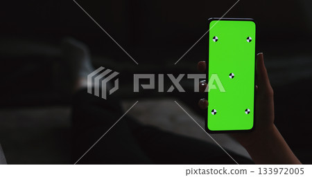 young woman lying on a couch and holding smartphone with vertical green screen 133972005