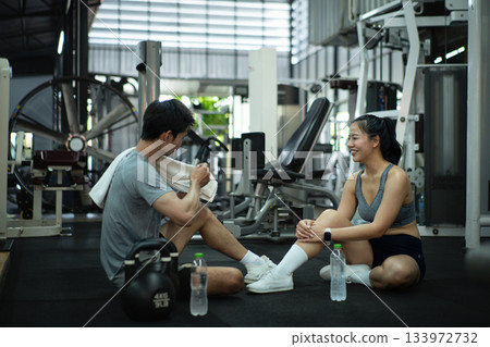 A trainer and a woman take a break after exercising, talking and cooling down together at the gym 133972732