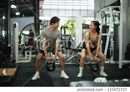 Fit and muscular man and woman focused on lifting a kettlebell during an exercise class Fit and muscular man and woman focused on lifting a kettlebell during an exercise class 133972737