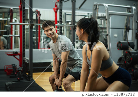 Fit and muscular man and woman focused on lifting a kettlebell during an exercise class Fit and muscular man and woman focused on lifting a kettlebell during an exercise class 133972738