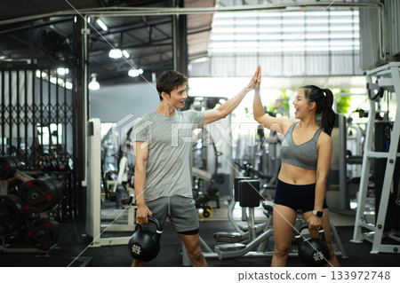 Fit and muscular man and woman focused on lifting a kettlebell during an exercise class Fit and muscular man and woman focused on lifting a kettlebell during an exercise class 133972748