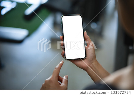 Women hand holding smart phone with blank white screen mockup in gym 133972754