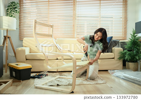 Young woman assembling new furniture at home with screwdriver, DIY home improvement 133972780