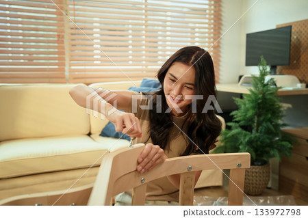 Young woman assembling new furniture at home with hex key, DIY home improvement 133972798