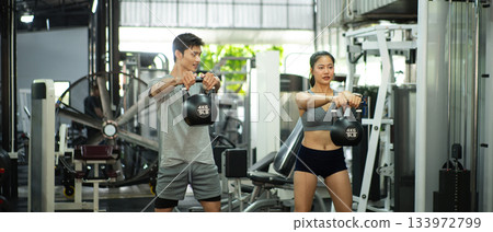 Fit and muscular man and woman focused on lifting a kettlebell during an exercise class Fit and muscular man and woman focused on lifting a kettlebell during an exercise class 133972799