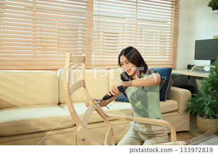 Young woman assembling new furniture at home with screwdriver, DIY home improvement Young woman assembling new furniture at home with screwdriver, DIY home improvement 133972819