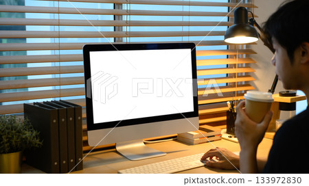 Creative man working on computer with blank screen and holding coffee cup Creative man working on computer with blank screen and holding coffee cup 133972830