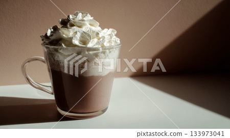 Hot chocolate in a glass mug topped with whipped cream, lit by soft warm sunlight. Cozy winter drink with a comforting sweet mood and delicious creamy texture. 133973041