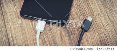 Black smartphone with charger cables on wooden background. Telephone charging concept 133973633
