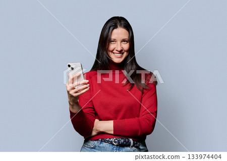 Beautiful smiling woman holding smartphone, on gray studio background Beautiful smiling woman holding smartphone, on gray studio background 133974404