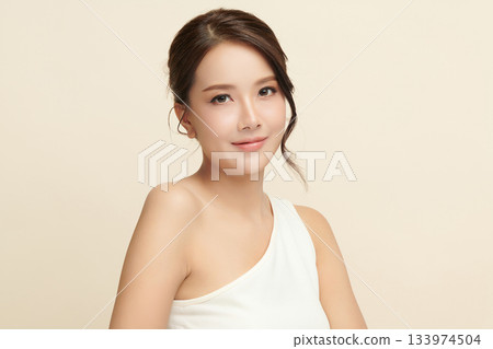 A beautiful young Asian woman with clean, fresh skin against a beige background. Skincare, facial treatment, cosmetology, beauty, and spa. An elegant portrait of an Asian woman. 133974504