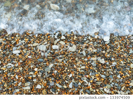 Sea wave washing over a shore covered with multicolored pebbles 133974509