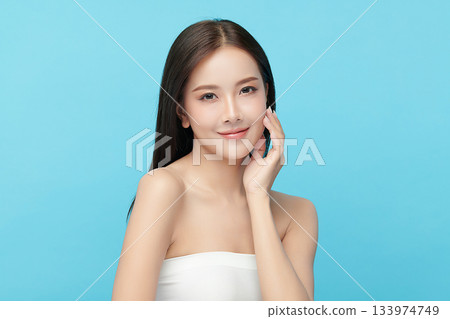 A beautiful young Asian woman with clean, fresh skin against a blue background. Skincare, facial treatment, cosmetology, beauty, and spa. An elegant portrait of an Asian woman. 133974749