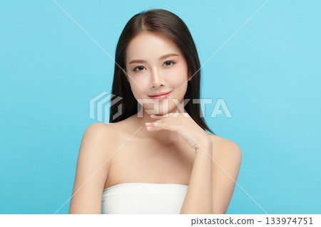 A beautiful young Asian woman with clean, fresh skin against a blue background. Skincare, facial treatment, cosmetology, beauty, and spa. An elegant portrait of an Asian woman. 133974751