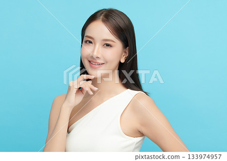 A beautiful young Asian woman with clean, fresh skin against a blue background. Skincare, facial treatment, cosmetology, beauty, and spa. An elegant portrait of an Asian woman. 133974957