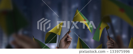 French Guiana flags in their hands on a blurred urban background French Guiana flags in their hands on a blurred urban background 133975996