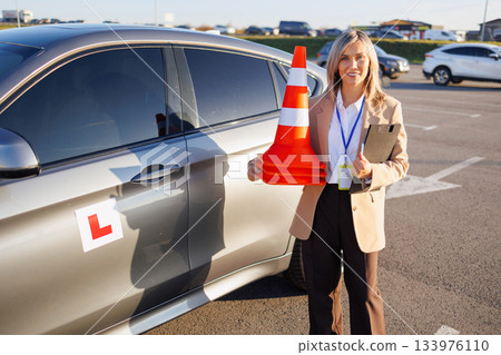 Driving Instructor Holding Cones Beside Training Car in Parking Lot Driving Instructor Holding Cones Beside Training Car in Parking Lot 133976110