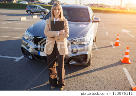 Instructor Standing by Learner Car with L Plate and Traffic Cones Instructor Standing by Learner Car with L Plate and Traffic Cones 133976111