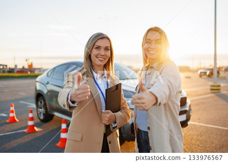 Driving instructor and learner celebrating successful driving practice with thumbs up Driving instructor and learner celebrating successful driving practice with thumbs up 133976567