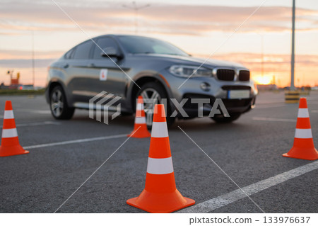 SUV navigating between traffic cones during driving practice at sunset on an empty parking lot 133976637