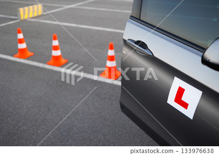 Learner driver vehicle approaching traffic cones during driving school training on an open asphalt area Learner driver vehicle approaching traffic cones during driving school training on an open asphalt area 133976638