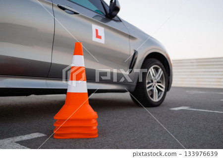 Stacked traffic cones beside learner driver SUV during driving practice on an open parking space 133976639