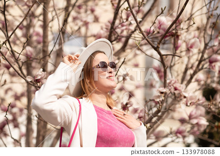 Magnolia spring woman: Woman smiles near magnolia flowers enjoying spring weather outdoors in sunlight. Magnolia spring woman: Woman smiles near magnolia flowers enjoying spring weather outdoors in sunlight. 133978088
