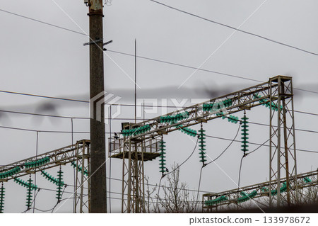 Workers inspect power lines and equipment on metal structures while clouds cover the sky in an electrical substation Workers inspect power lines and equipment on metal structures while clouds cover the sky in an electrical substation 133978672
