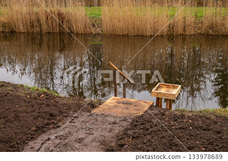 Wooden steps provide access to a river with a small platform nearby. Bare trees and tall grass reflect in the water in the afternoon Wooden steps provide access to a river with a small platform nearby. Bare trees and tall grass reflect in the water in the afternoon 133978689