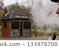 A person smokes from an electronic device while standing near a small coffee kiosk outside during a cloudy day 133978700