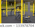 A variety of fitness equipment stands ready for use in an open park, showing benches and bars for exercise during a cloudy day 133978704