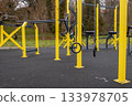 People can use yellow workout stations in an outdoor gym located in a park with trees on a cloudy day in autumn 133978705