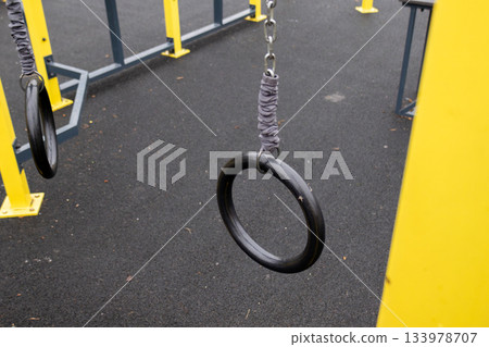 Children enjoy swinging on gym rings in a park playground during afternoon hours. Kids engage in active play and exercise Children enjoy swinging on gym rings in a park playground during afternoon hours. Kids engage in active play and exercise 133978707