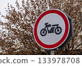 A sign shows that motorcycles are not allowed, placed near a tree without leaves, indicating winter time and location in a city 133978708