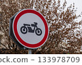 A round traffic sign shows a motorcycle symbol with a red circle around it, placed near bare trees on a cloudy day 133978709