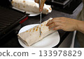 Hands cutting fresh shawarma wrap with knife on plate 133978829