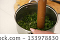 Chef crushing fresh green onions in stainless steel pot 133978830