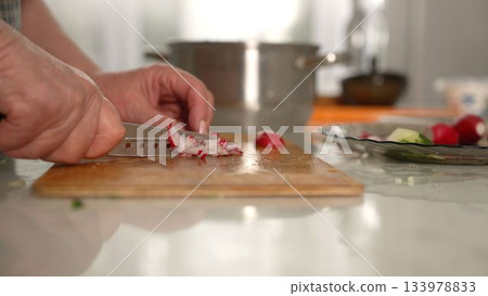 Chef slicing fresh radishes on wooden cutting board 133978833