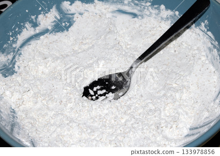 Close up of white flour in a bowl with a silver spoon Close up of white flour in a bowl with a silver spoon 133978856