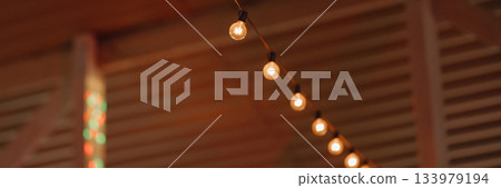 Banner warm string lights hanging in wooden interior with blurred background 133979194